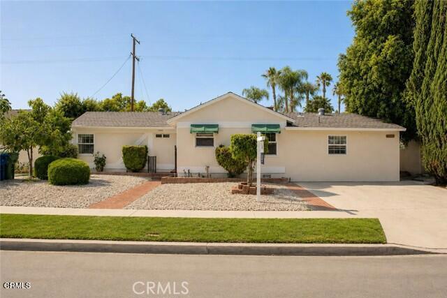 Single-story beige house with green awnings, gravel landscaping, and palm trees behind it.