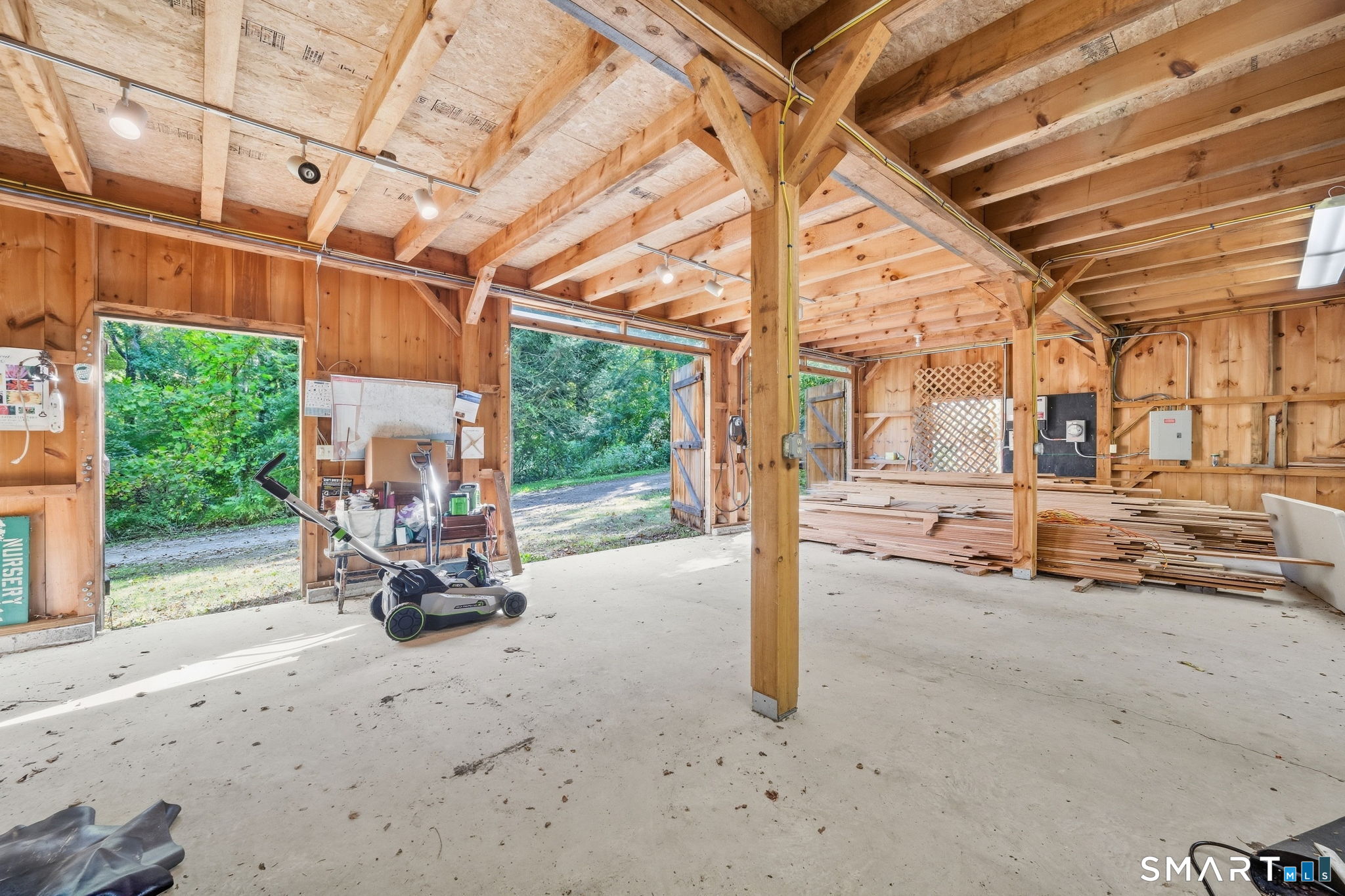 Timber-framed workshop with open doors, stacked lumber, and a lawn mower.