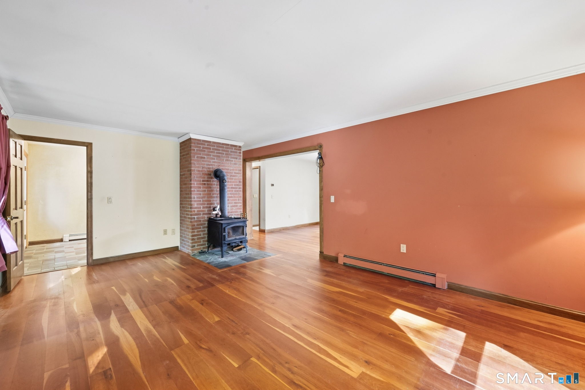 Unfurnished living room with polished hardwood floors and a wood-burning stove against a brick hearth.