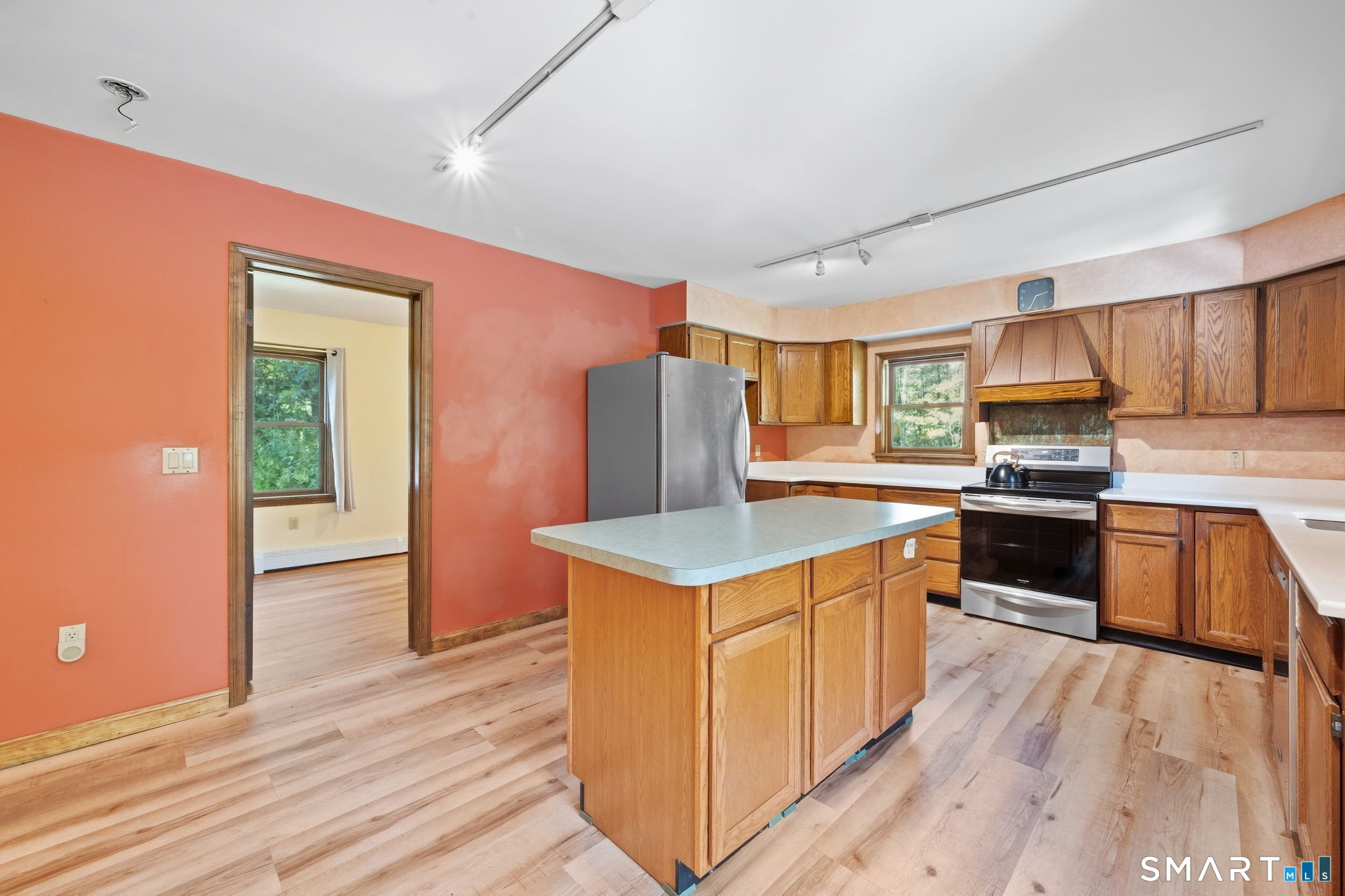 Kitchen with wood cabinets, a large central island, stainless steel appliances, and light wood-look flooring.