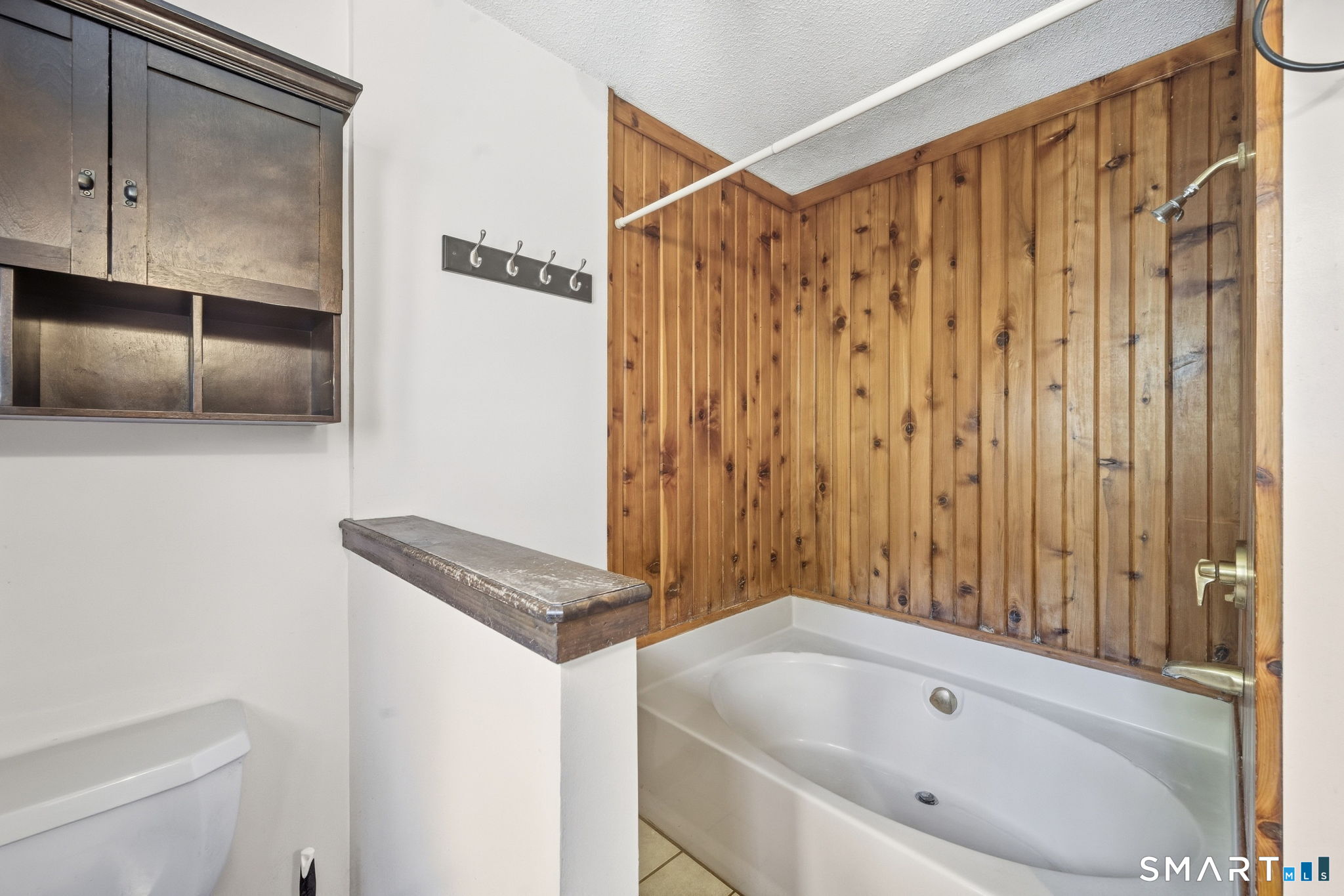 Bathroom with a jetted tub, wood-paneled surround, glass shower screen, and built-in cabinetry.
