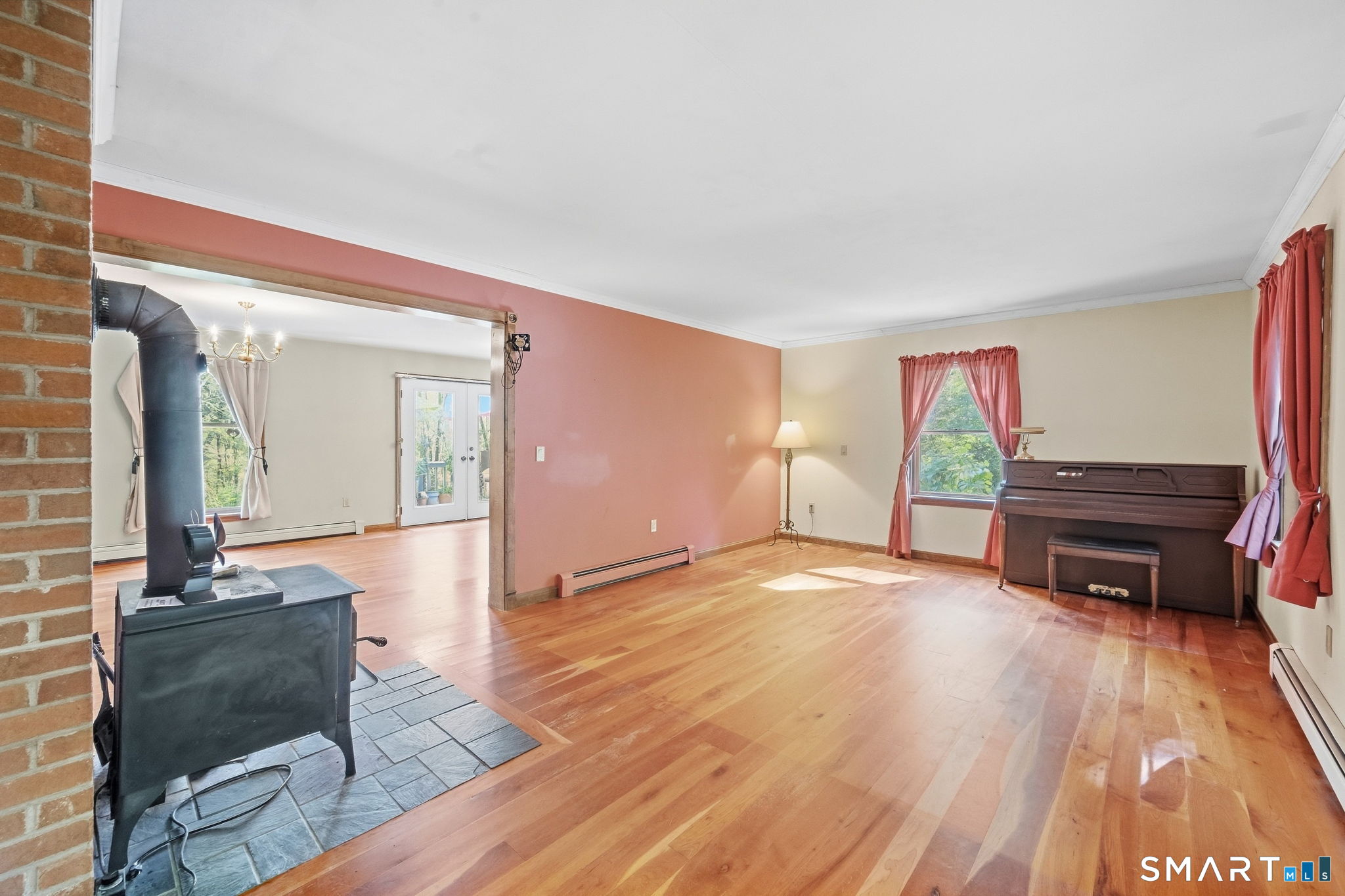 Living room with a wood stove, polished hardwood floors, and a dark upright piano.