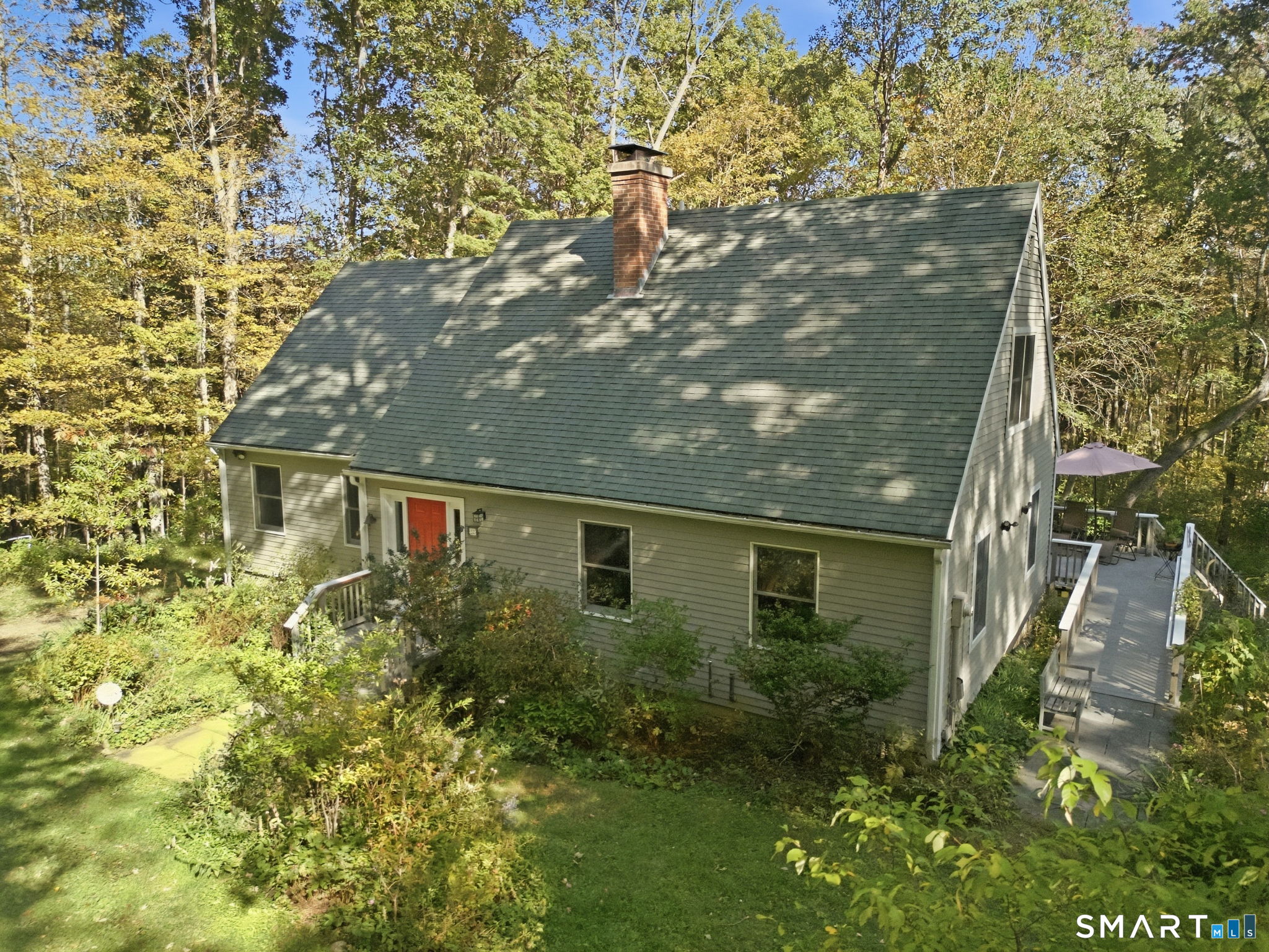 Gray-sided house with a steep roof and red door, surrounded by autumn trees and a wooden deck.