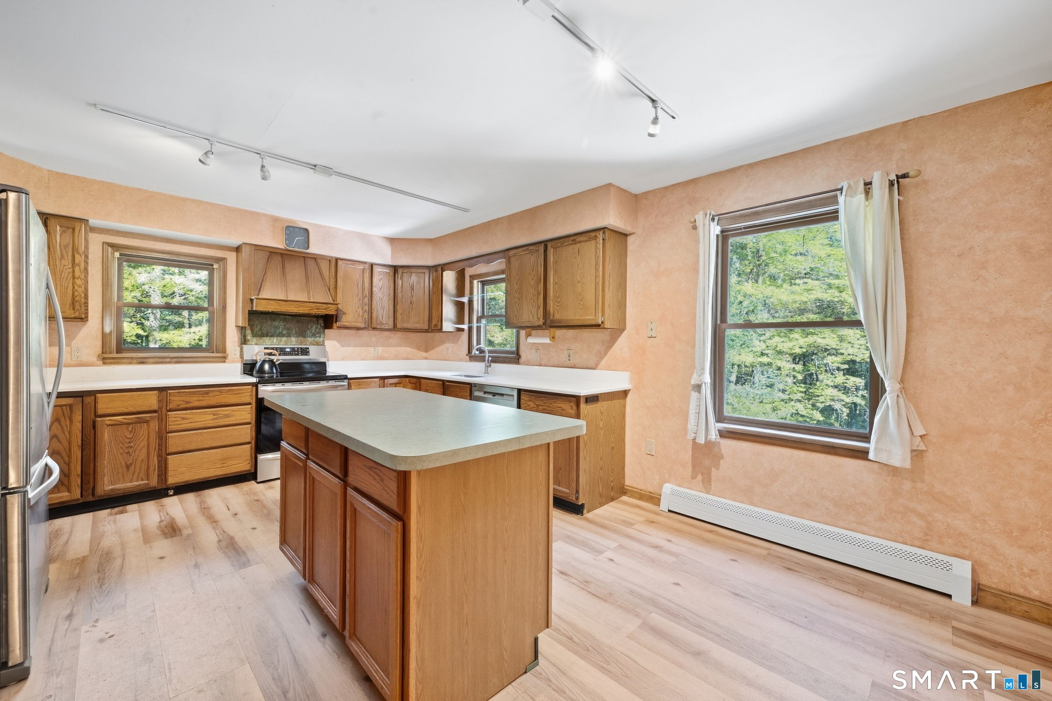 Kitchen with warm wood cabinets, a central island, and windows overlooking leafy trees.