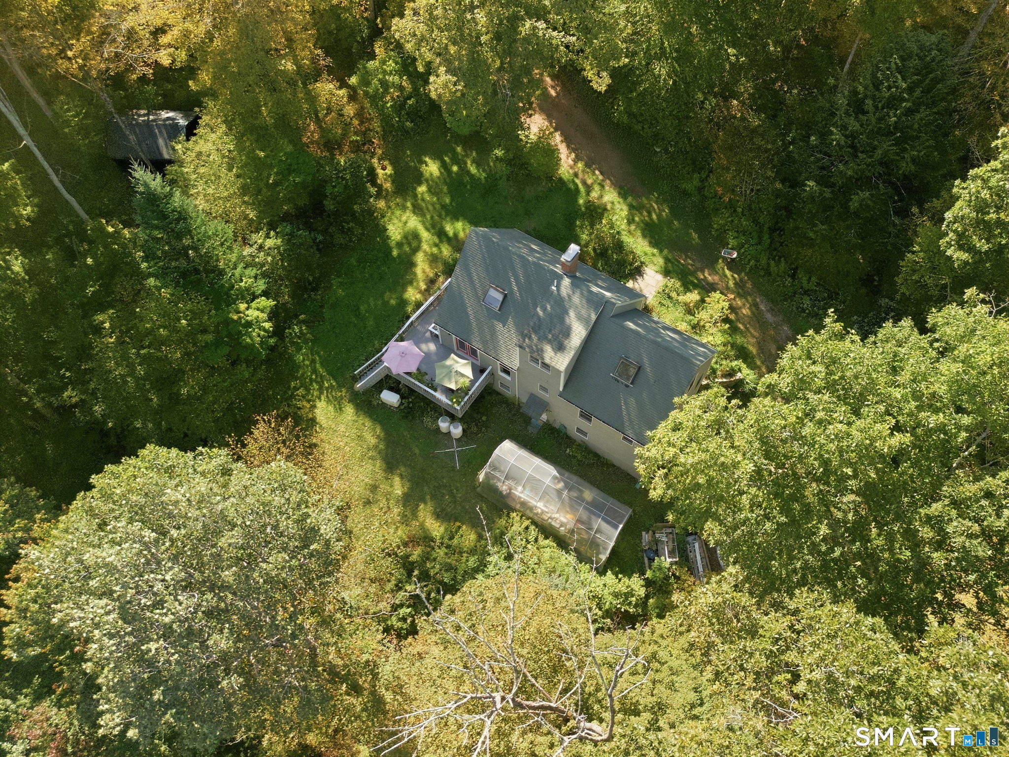 Aerial view of a house in a wooded yard with a deck and greenhouse.