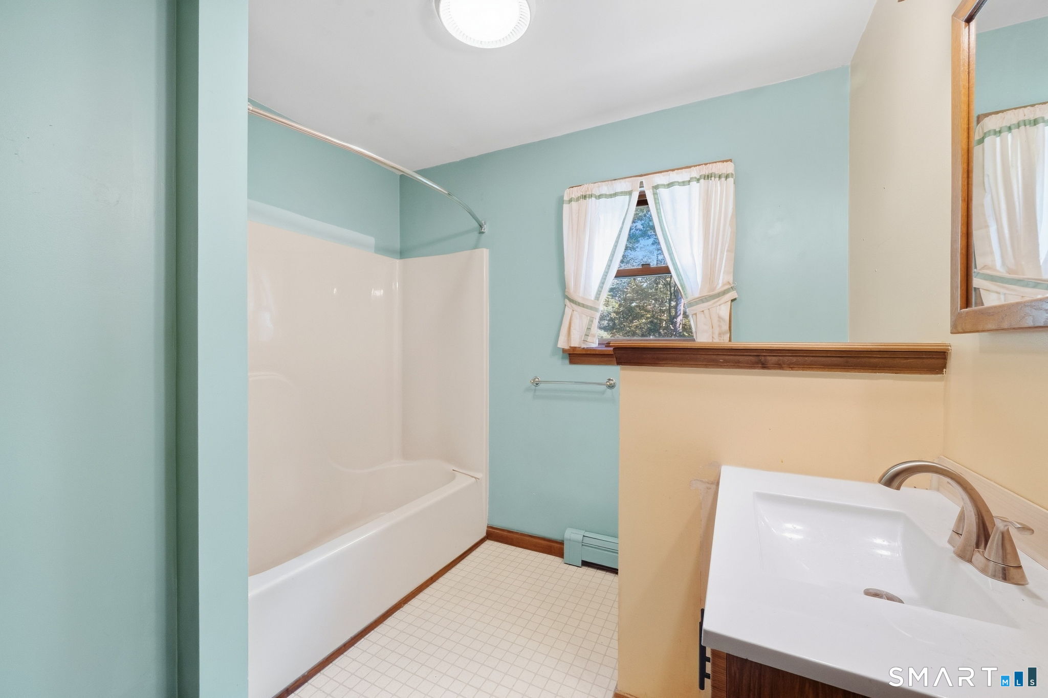 Bathroom with a white tub and shower, aqua walls, curtained window, and sink vanity.