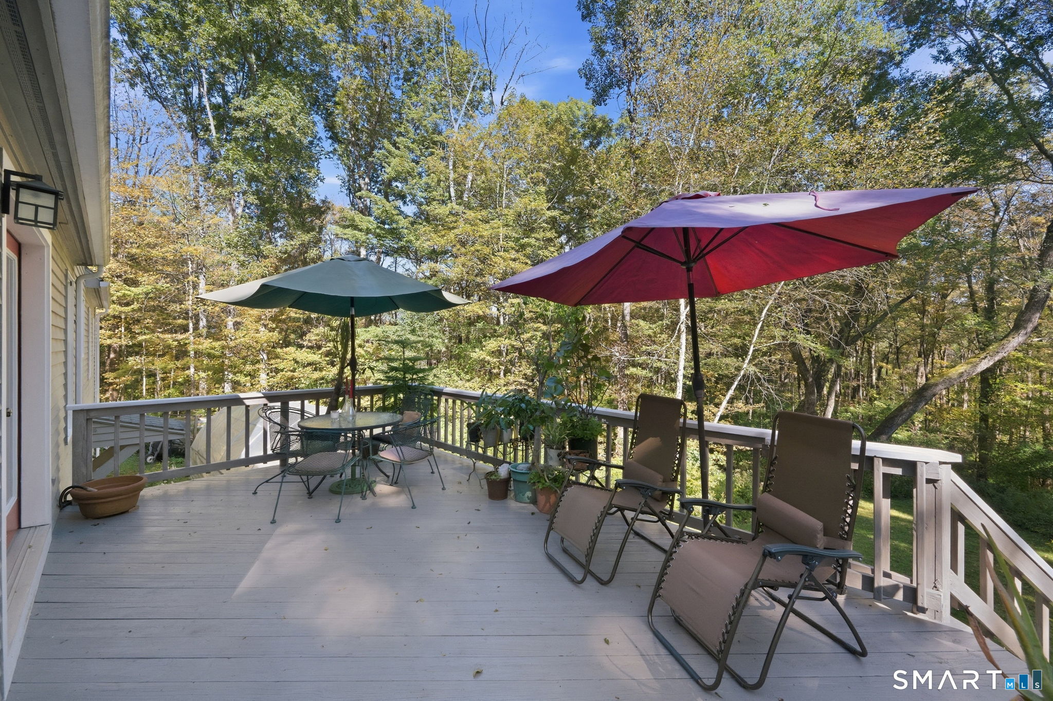 Furnished deck with two umbrellas and lounge chairs overlooking autumn woods.