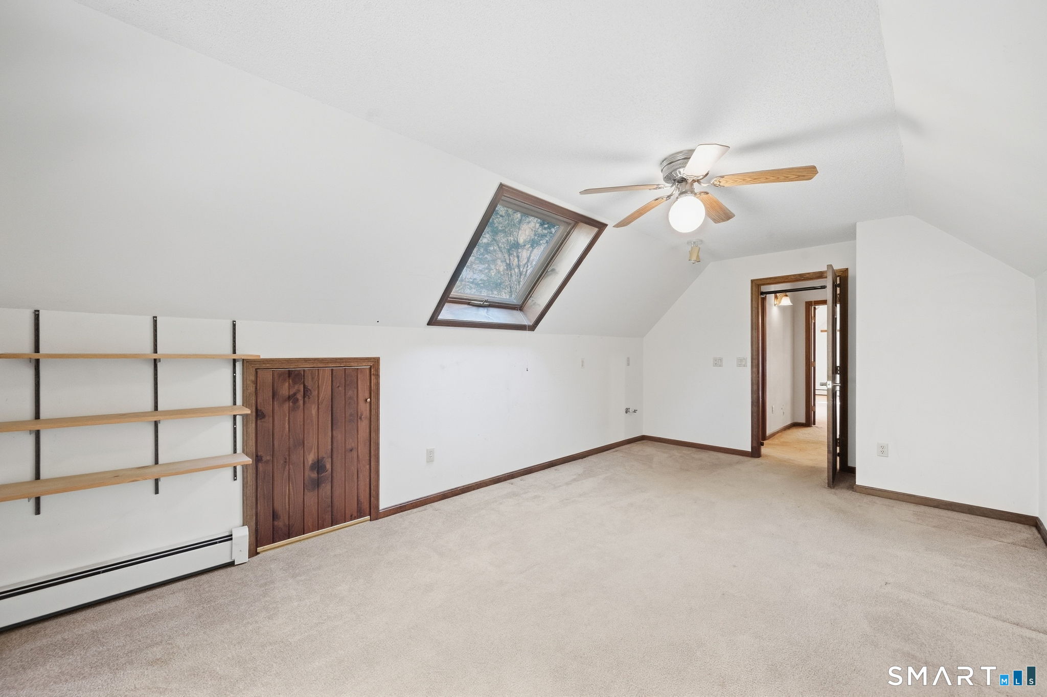 Vacant carpeted room with a sloped ceiling, skylight, ceiling fan, and built-in shelves.
