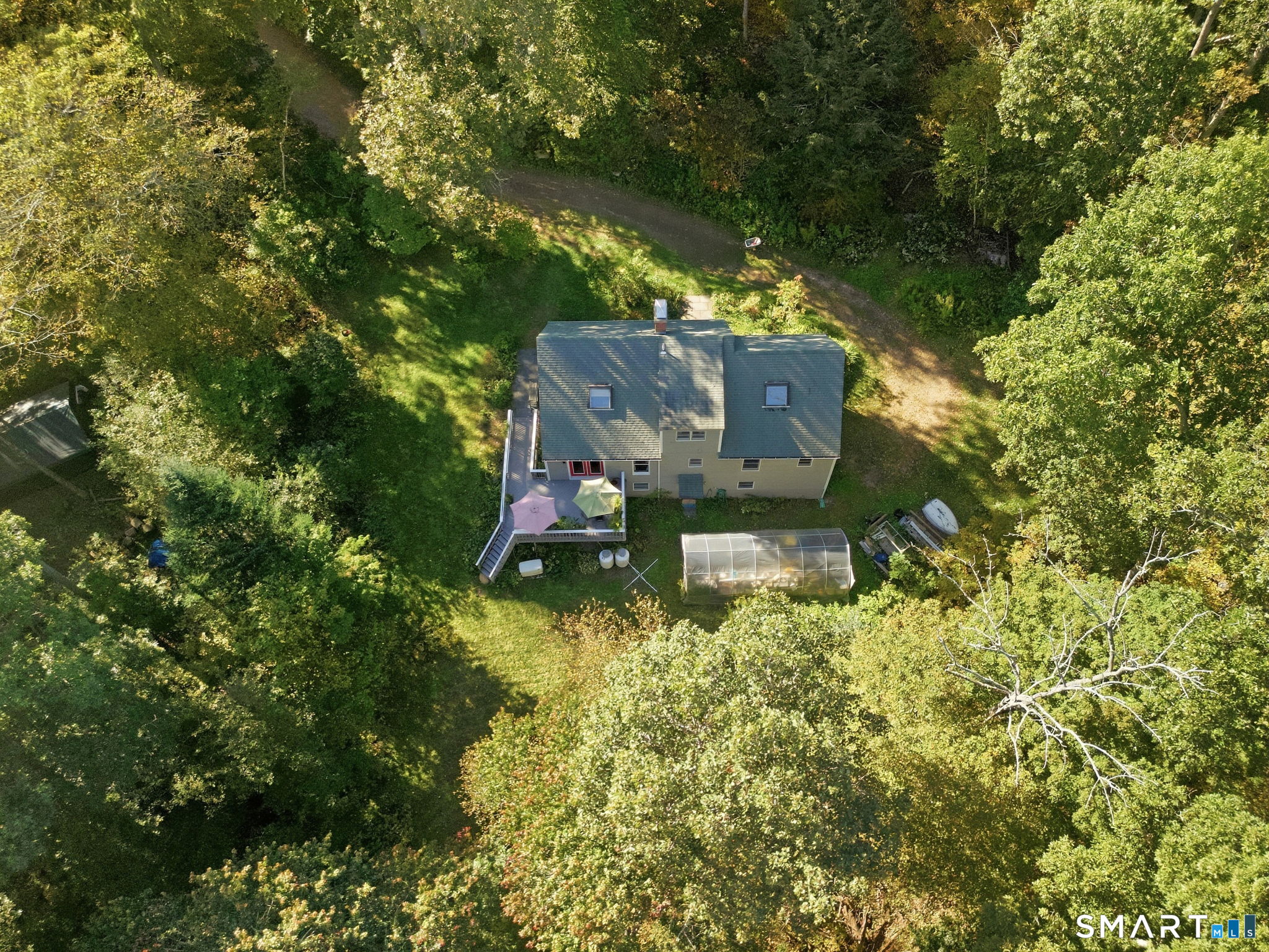 Aerial view of a house in a wooded yard, with a deck and greenhouse.
