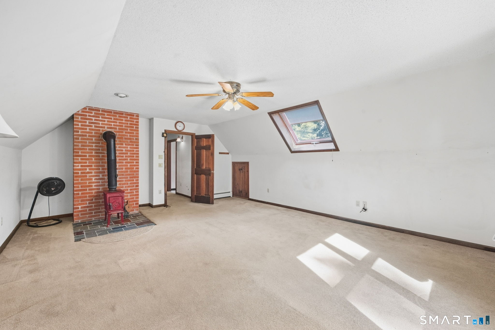 Attic living area with a red wood stove, brick hearth, and skylight.