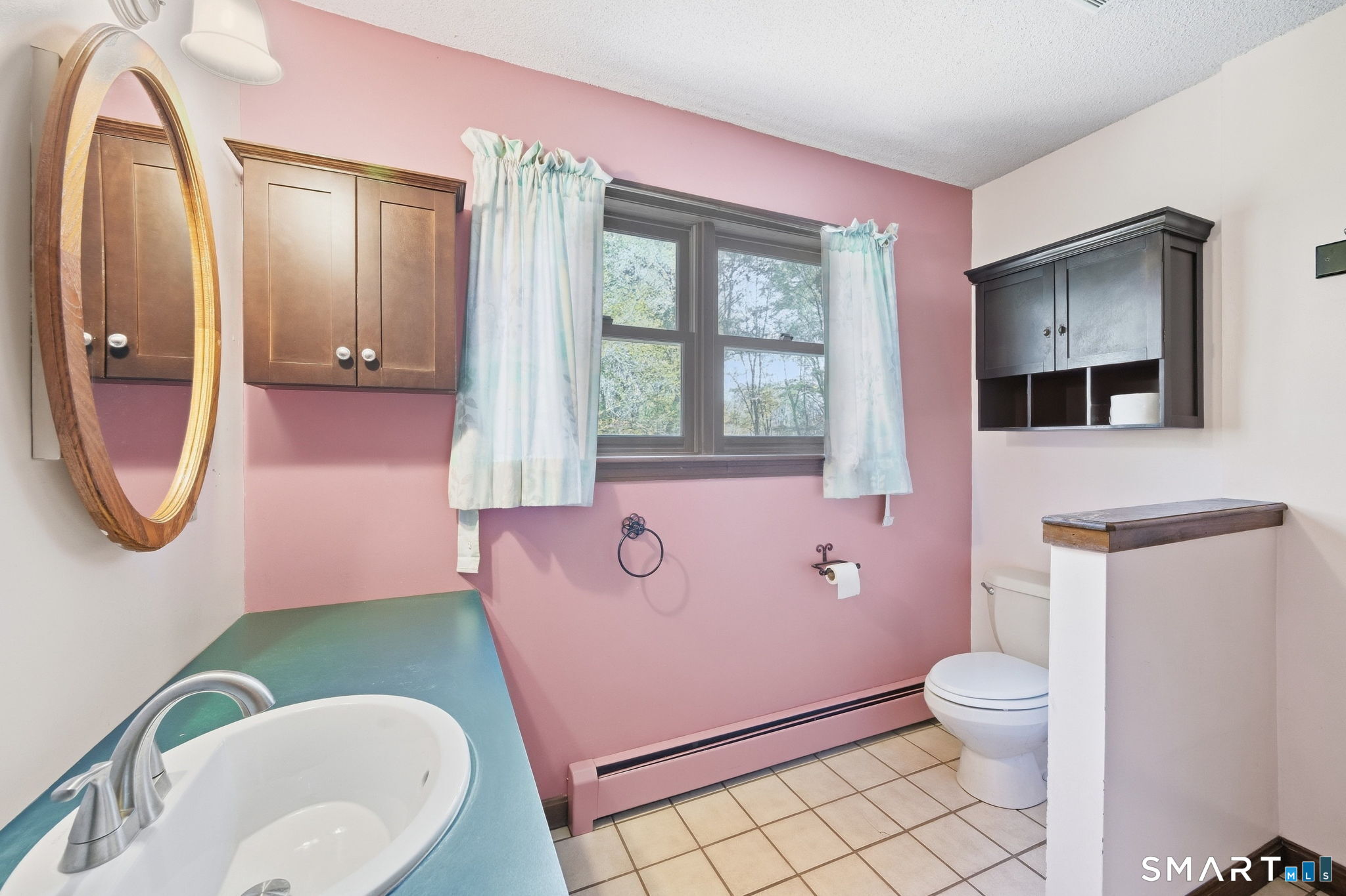 Bathroom with pink walls, teal vanity countertop, dark cabinets, and a window above the toilet.