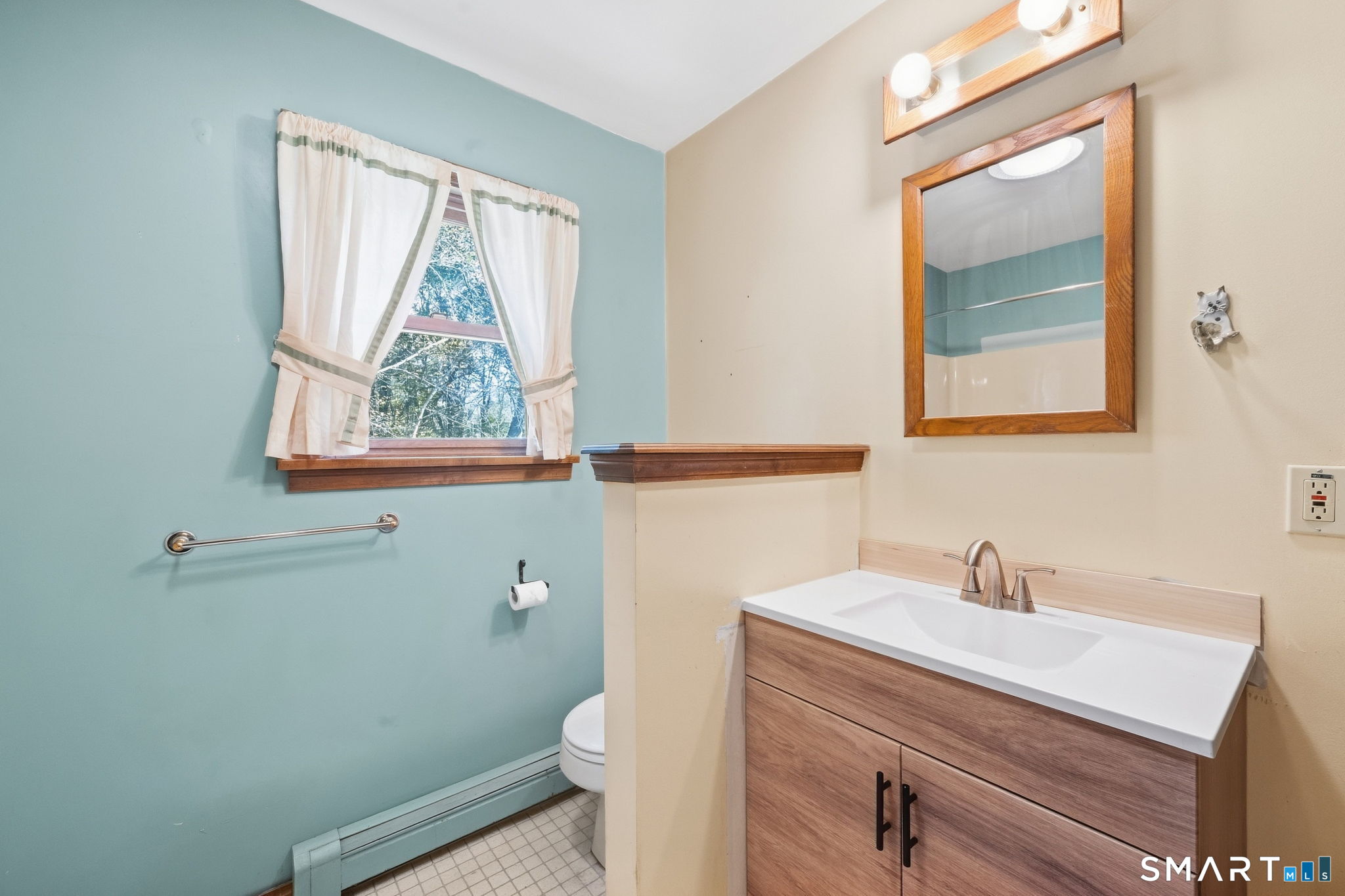 Bathroom with a wood vanity, framed mirror, and curtained window.