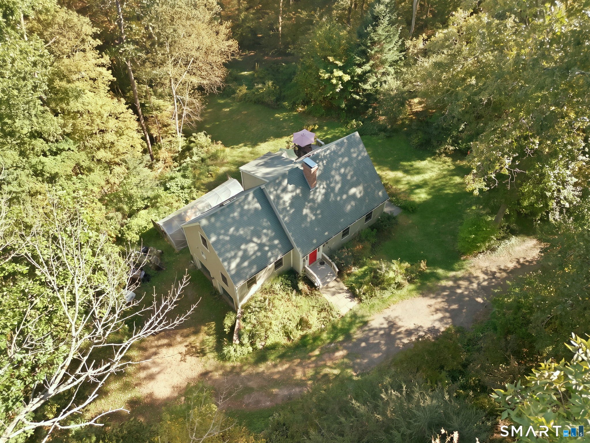 Aerial view of a wooded property with a detached home, screened porch, and gravel driveway.
