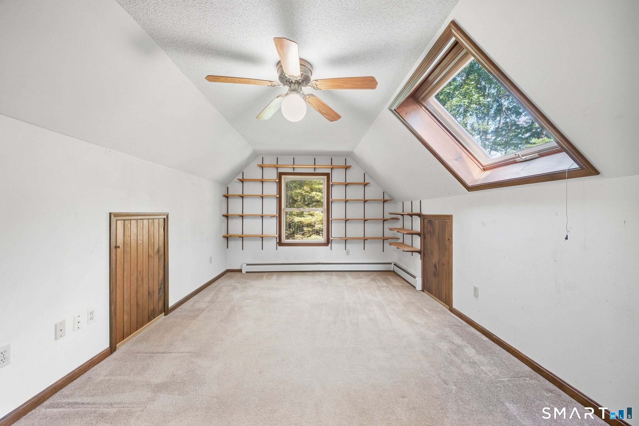 Empty carpeted room with built-in wooden shelves, a vaulted ceiling, and a large skylight.