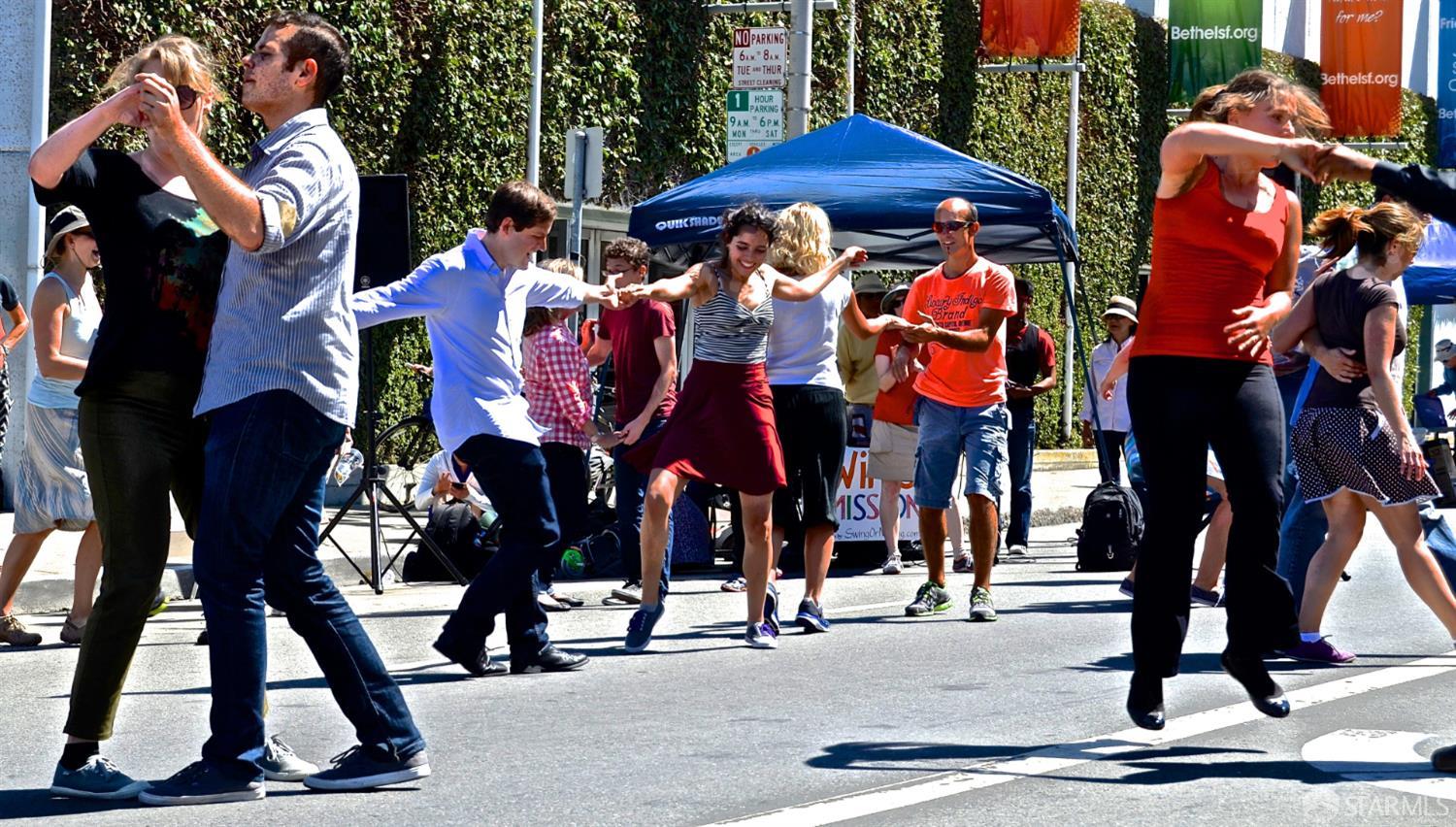 People dance together in the street at a sunny outdoor gathering.