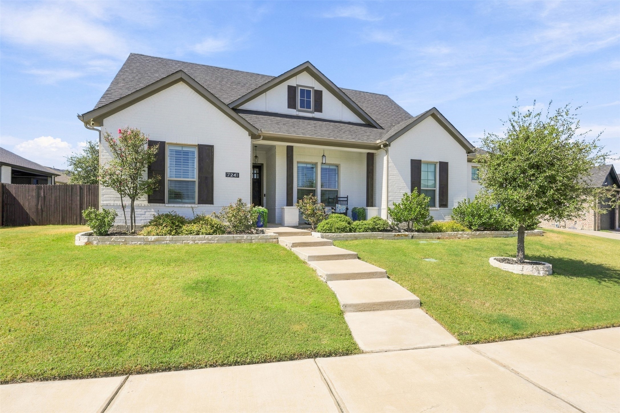 White two-story house with dark shutters, landscaped front yard, and a curved walkway.