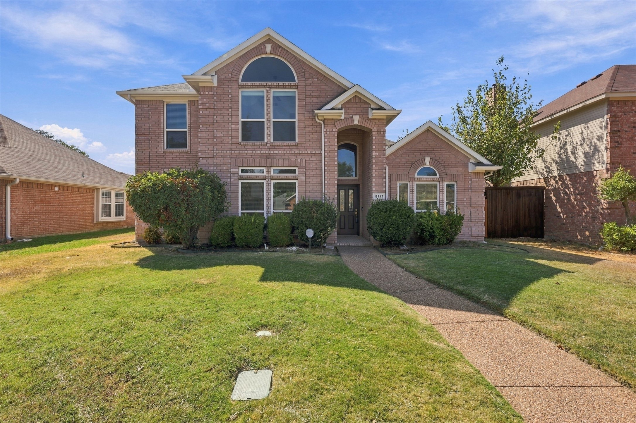 Two-story brick house with arched windows, trimmed shrubs, and a walkway across the front lawn.