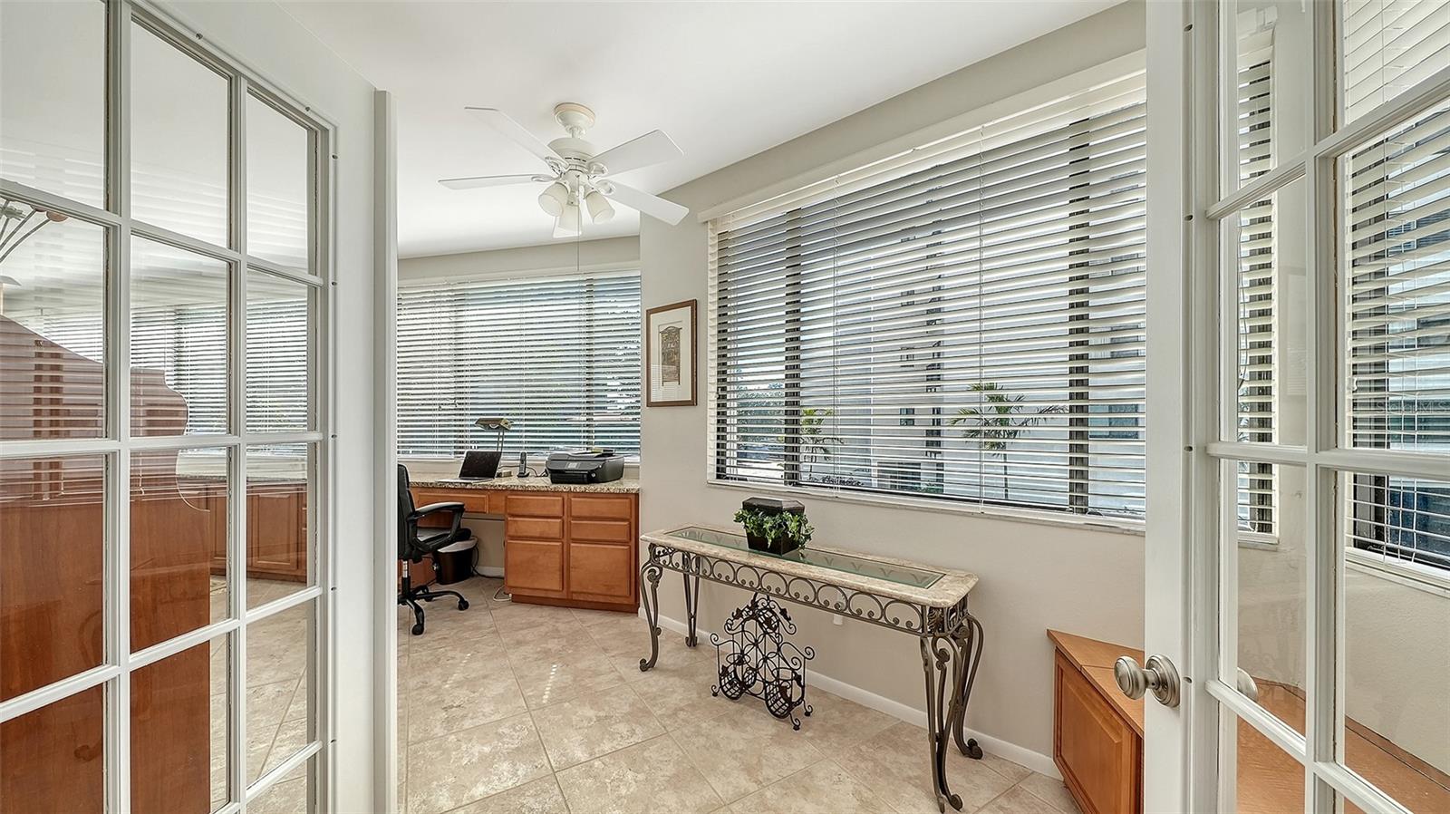 Bright office with built-in wood desk, tiled floor, and large windows overlooking water.