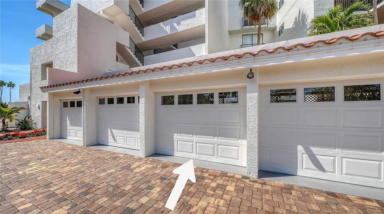 Condominium exterior with white garage doors, terracotta-tile awning, and a driveway arrow pointing to one garage.