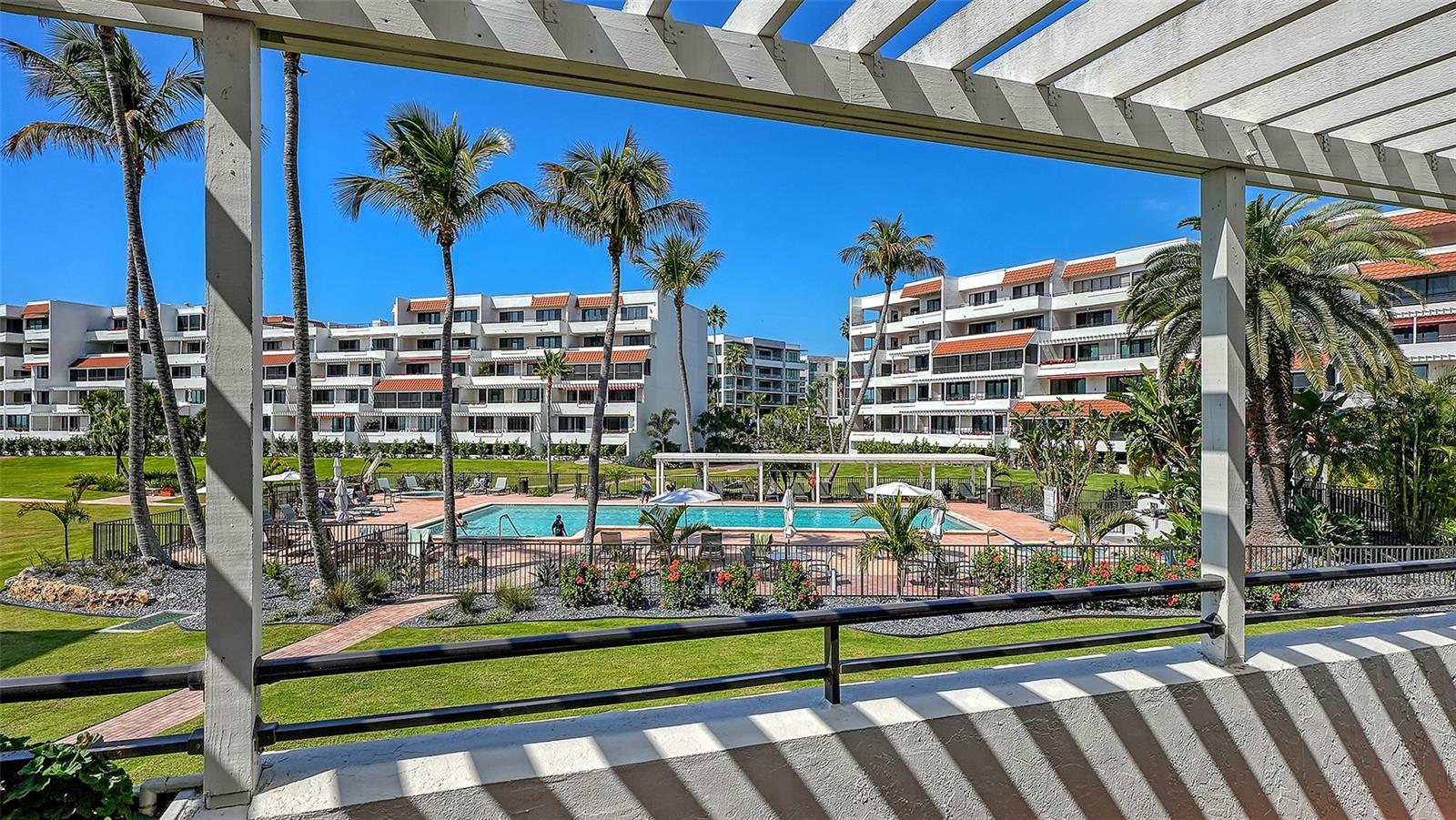 Community pool and palm-lined condominium buildings viewed from a covered balcony.