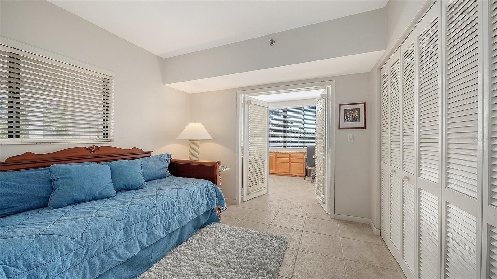 Bedroom with a blue daybed, louvered closets, and open doors to an adjoining room.