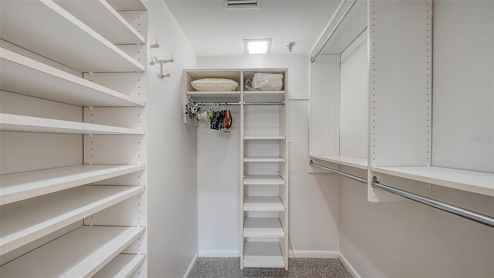 Walk-in closet with extensive white shelving, hanging rods, and carpeted floor.
