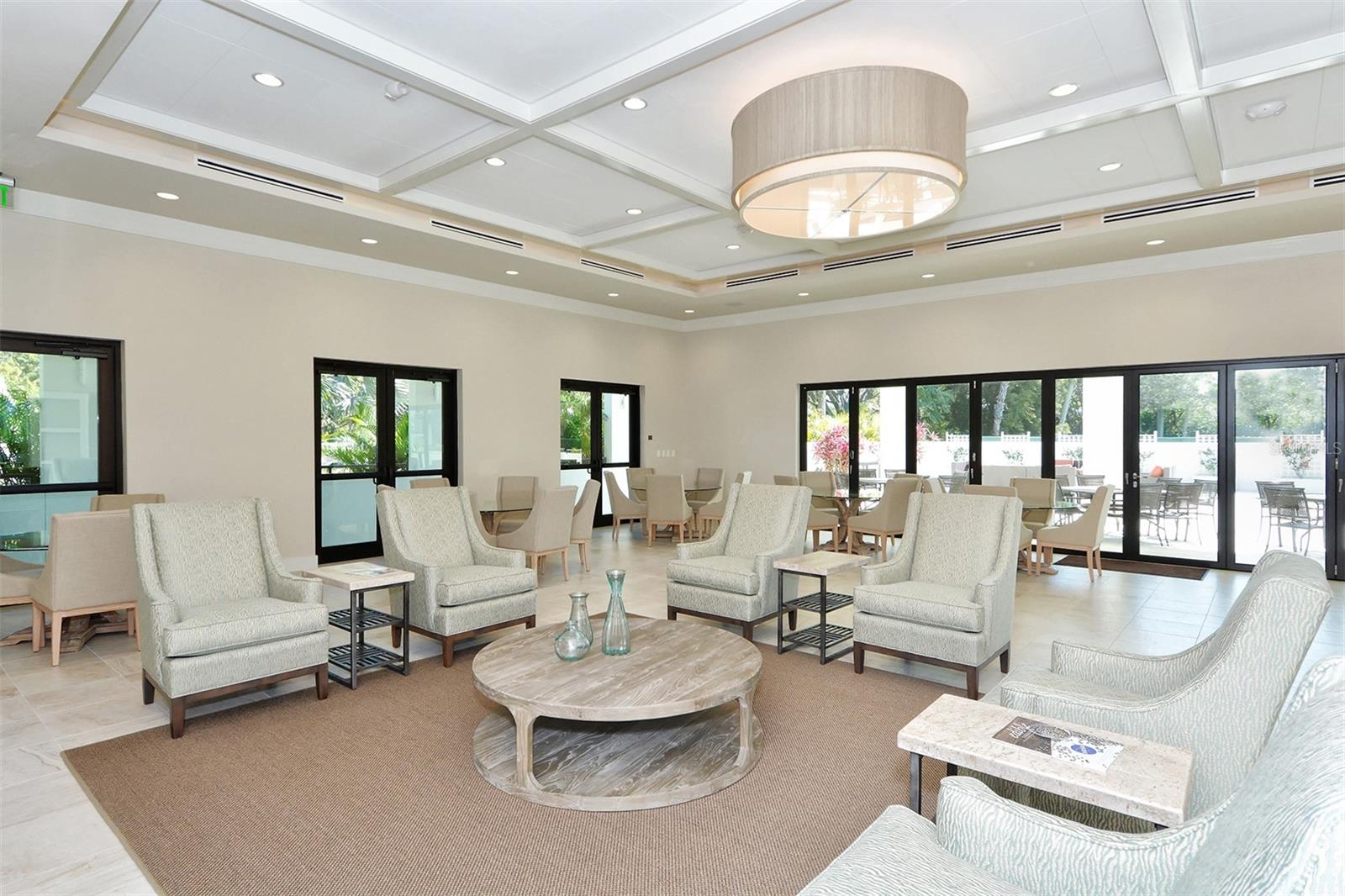 Furnished common lounge with pale armchairs, a round coffee table, and glass doors to the patio.