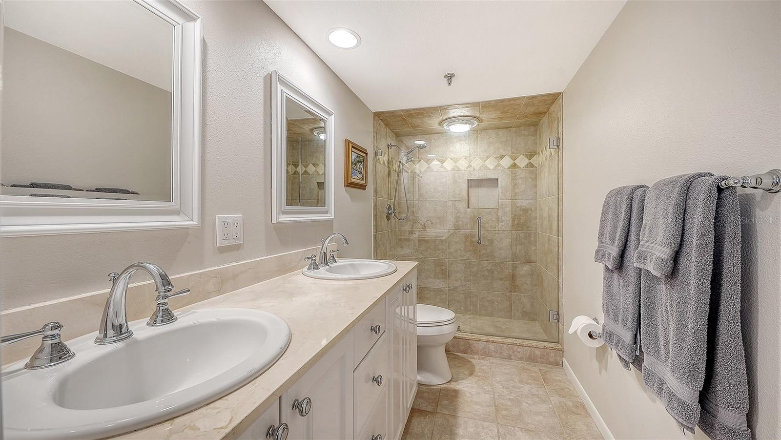 Bathroom with double-sink vanity and glass-enclosed tiled shower.
