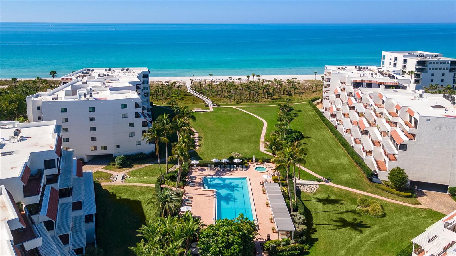Aerial view of beachfront condominiums, a central swimming pool, landscaped grounds, and the Gulf of Mexico.