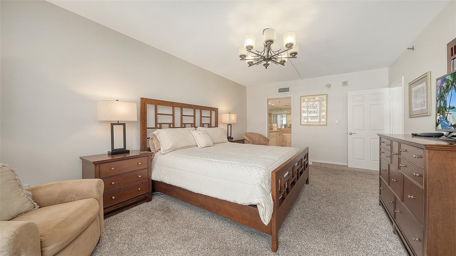Furnished bedroom with a large wooden bed, white bedding, matching dressers, and beige carpet.