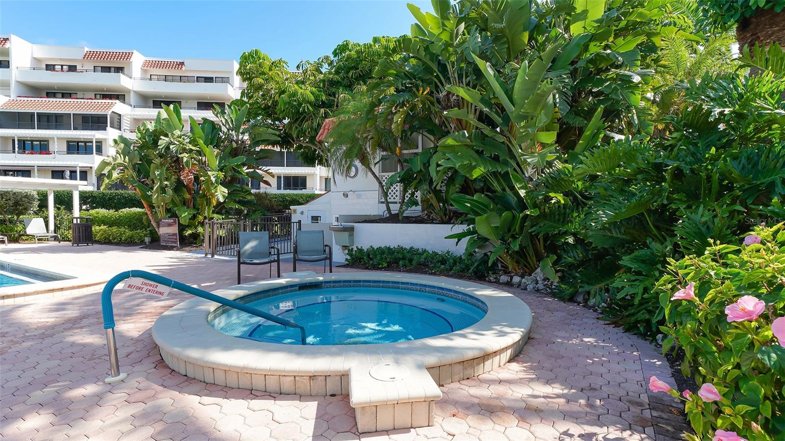Condominium spa beside a swimming pool, surrounded by tropical landscaping and patio seating.
