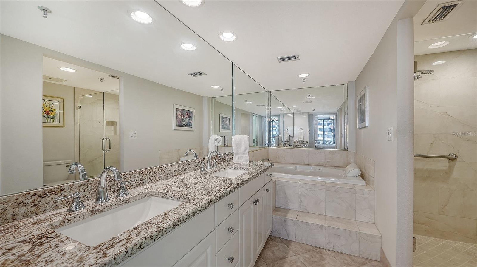 Bathroom with a long granite double-sink vanity, built-in soaking tub, and glass-enclosed shower.