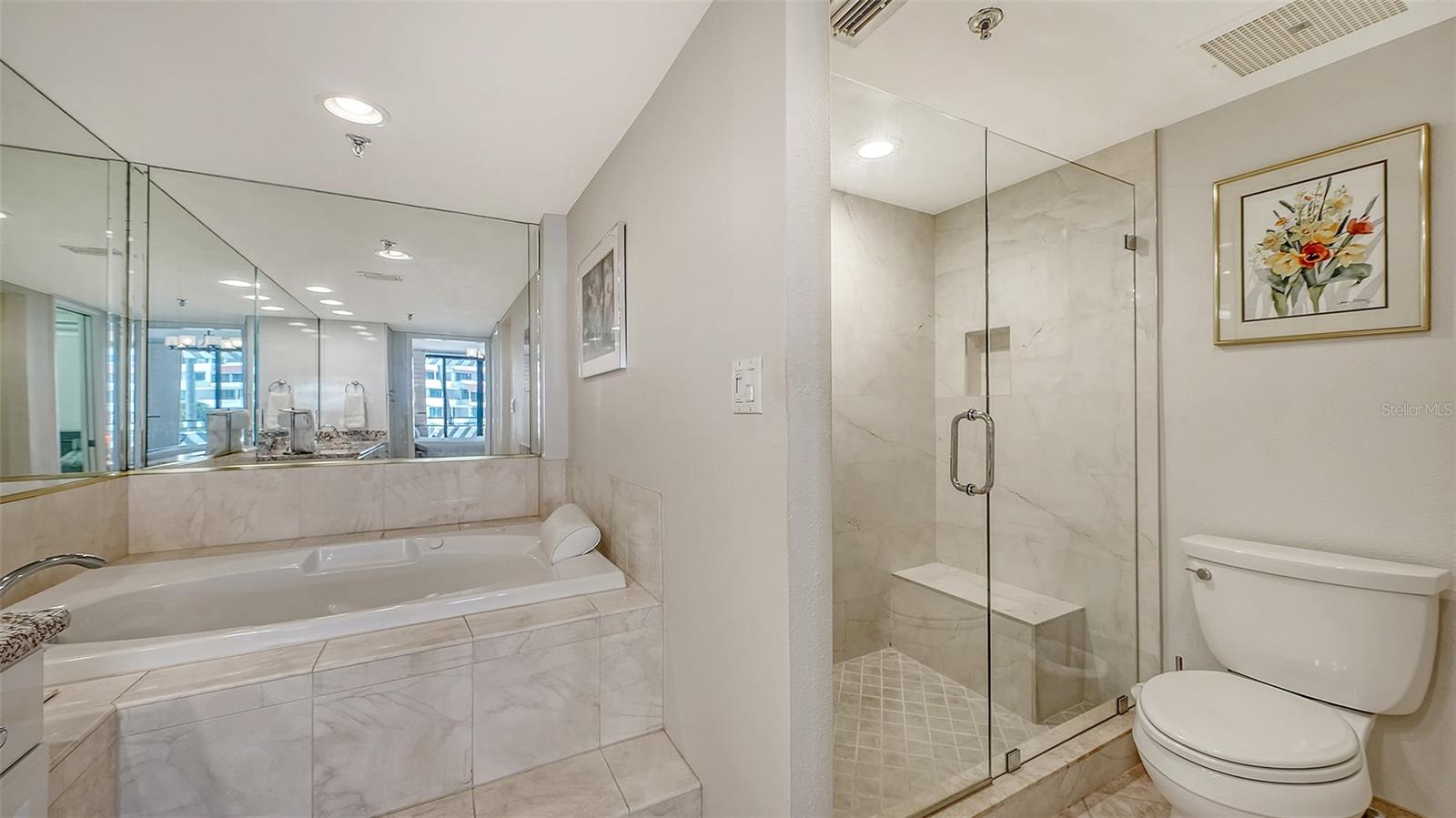 Marble bathroom with a built-in soaking tub, glass shower, and toilet.