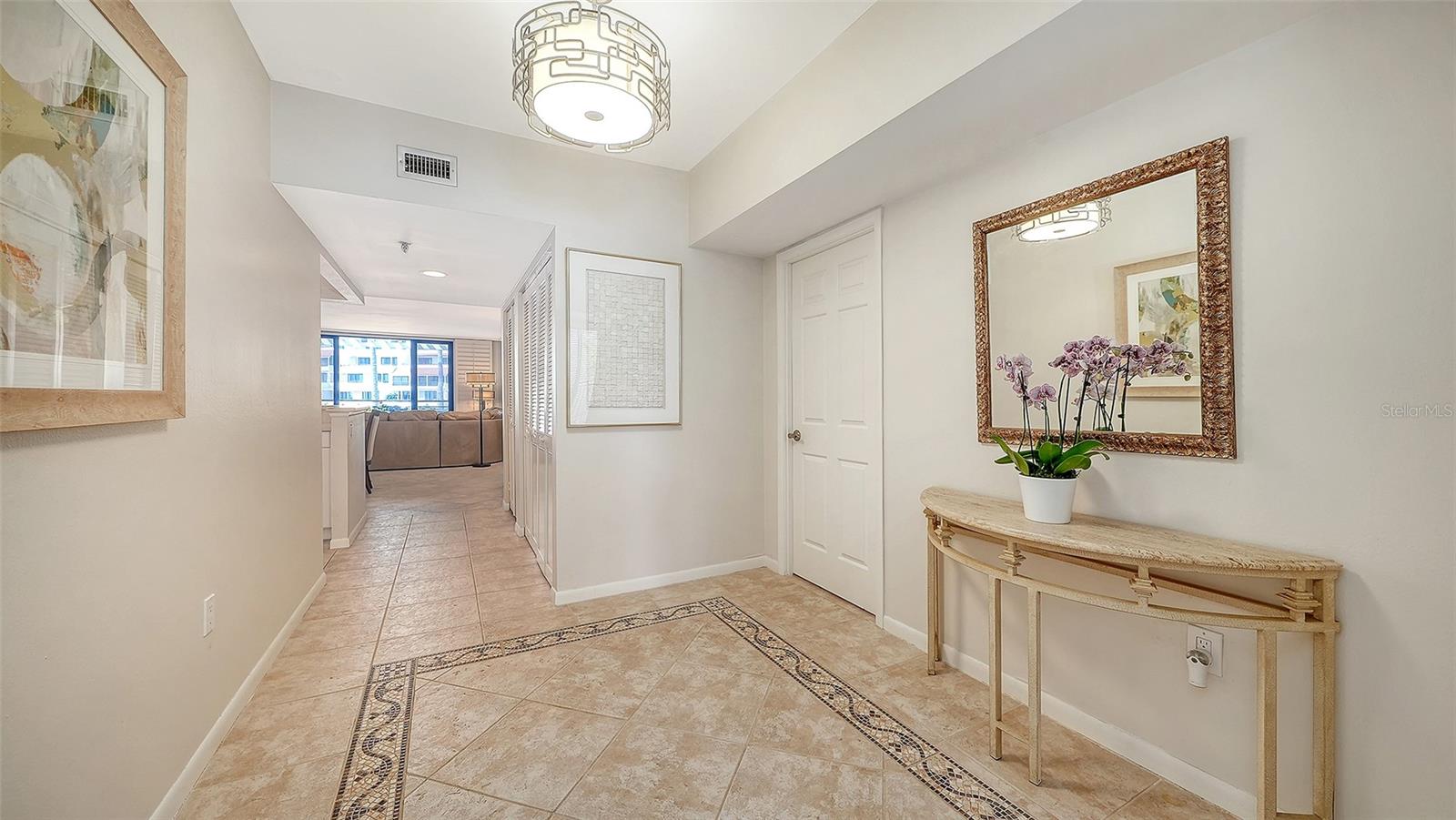 Condominium entry hall with patterned tile floor, orchid-topped console, and living room beyond.