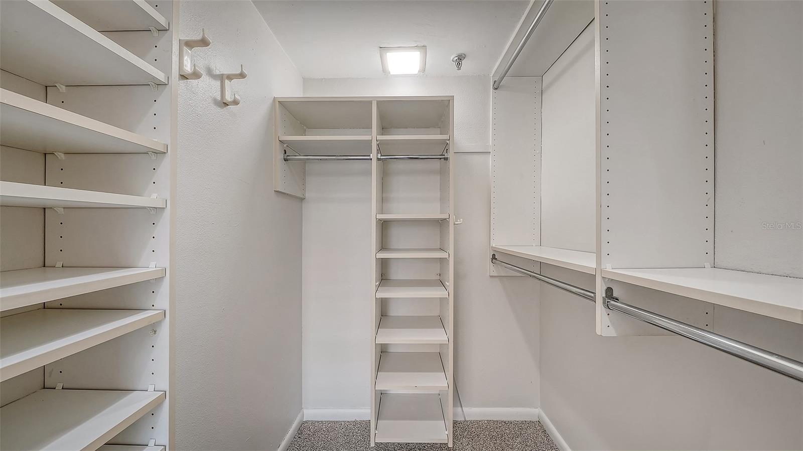 Walk-in closet with white built-in shelves and hanging rods.