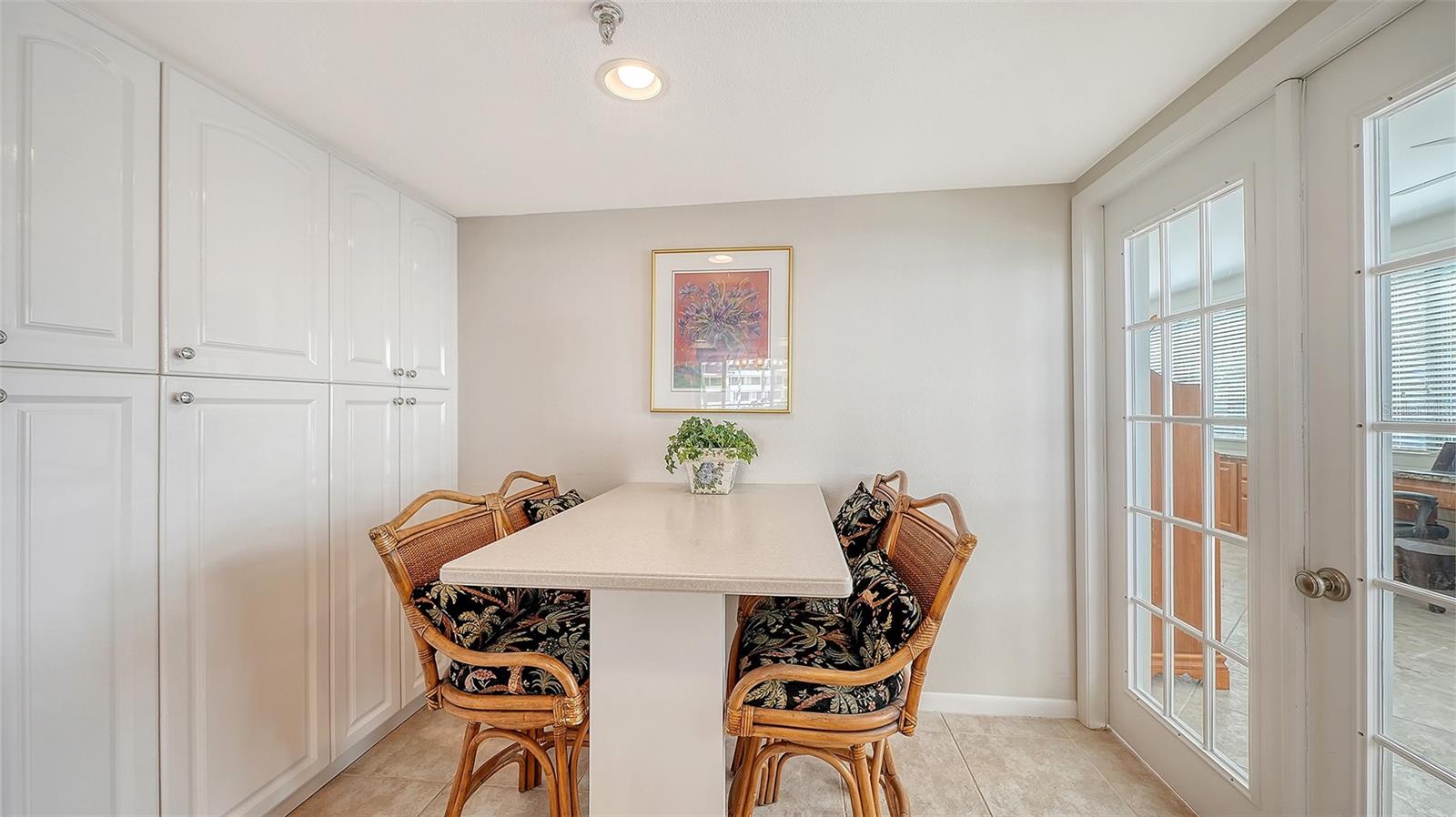 Dining nook with a white table, wicker chairs, built-in cabinets, and glass doors to the outdoor area.