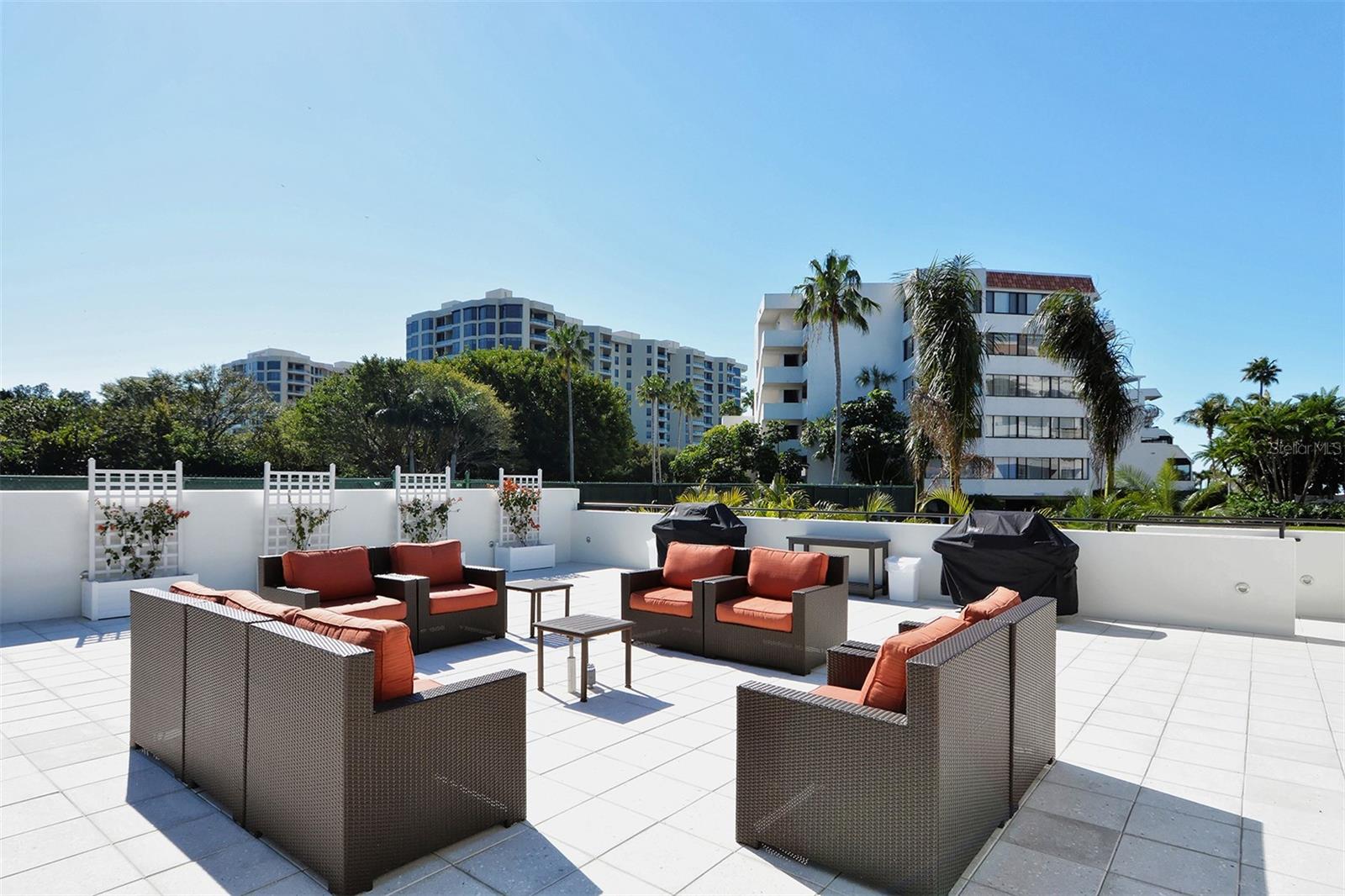 Furnished condo terrace with orange-cushioned lounge seating, tiled floor, and palm trees.