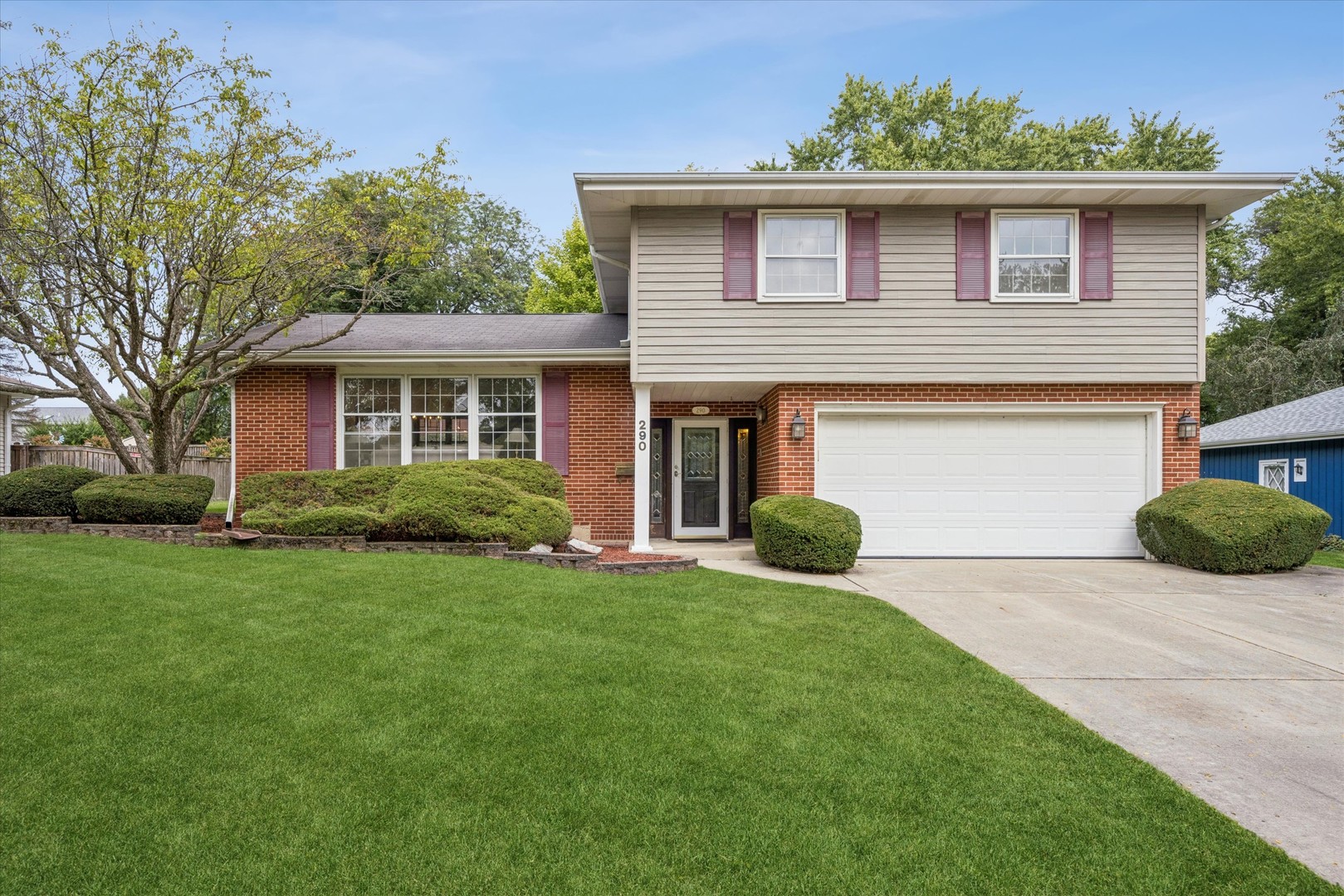 Two-story brick and siding home with burgundy shutters, attached garage, and broad green lawn.