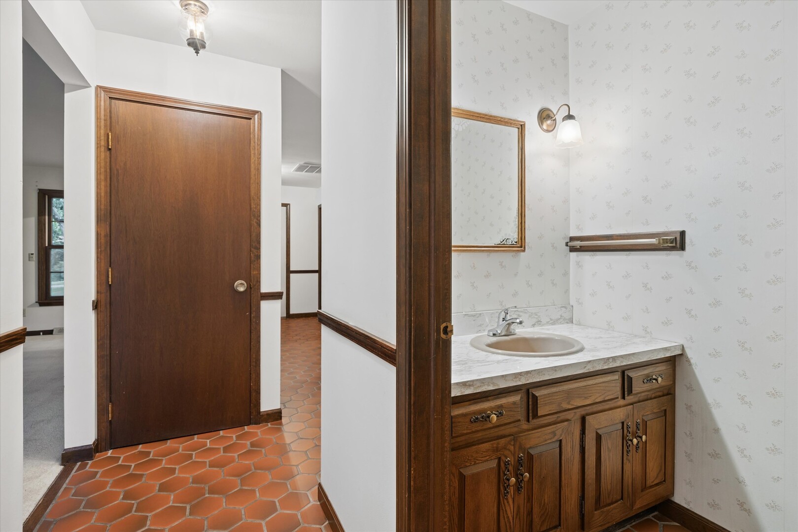Bathroom vanity with dark wood cabinetry, floral wallpaper, and terracotta hexagonal tile flooring.