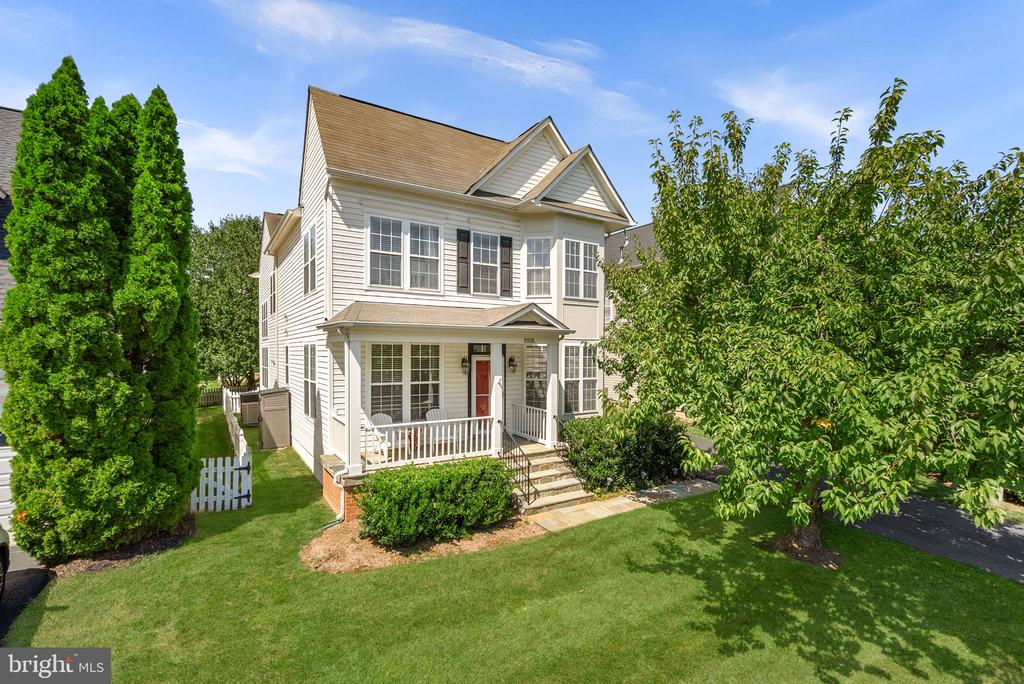 White two-story house with a covered porch, red front door, and mature trees.