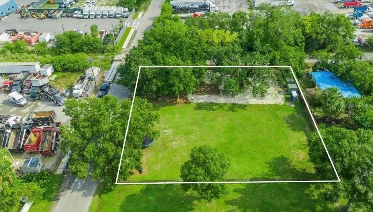 Vacant grassy parcel outlined in white beside commercial vehicle and equipment yards.