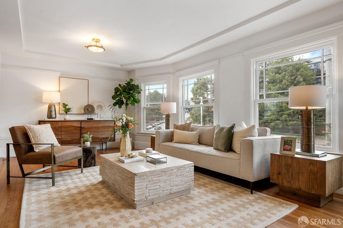 Staged living room with a beige sofa, sculptural coffee table, and large street-facing windows.