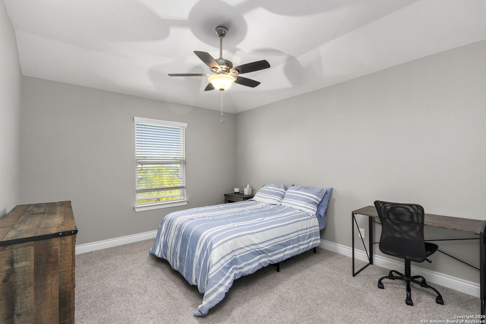 Bedroom with a blue-and-white striped bed, ceiling fan, and desk beside the window.