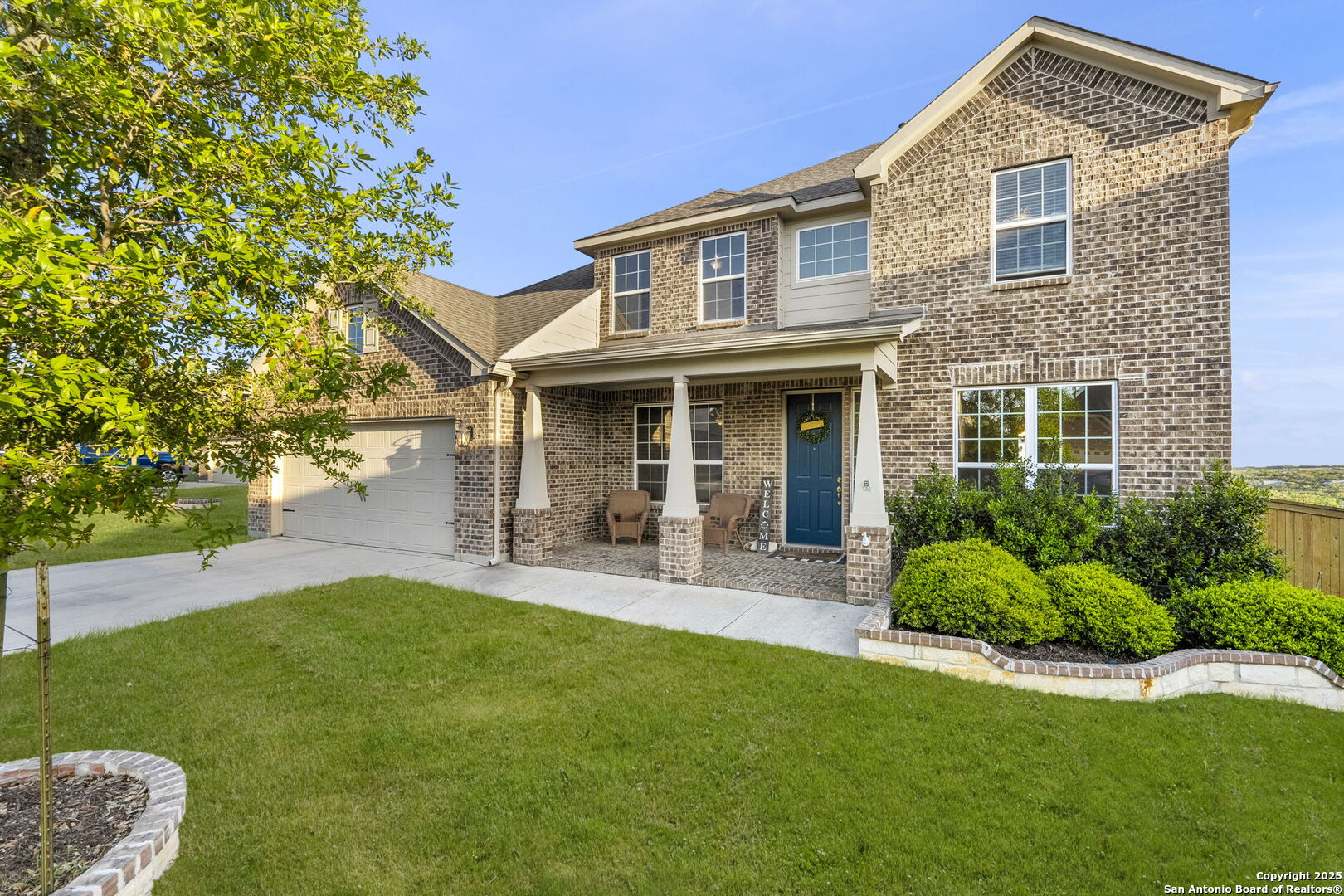 Two-story brick home with a covered porch, blue front door, attached garage, and landscaped lawn.