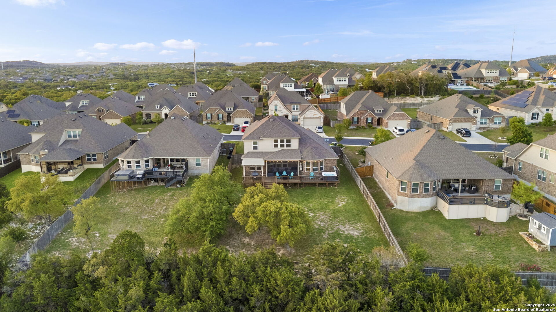 Aerial view of a brick home with a raised deck and fenced backyard among neighboring houses.