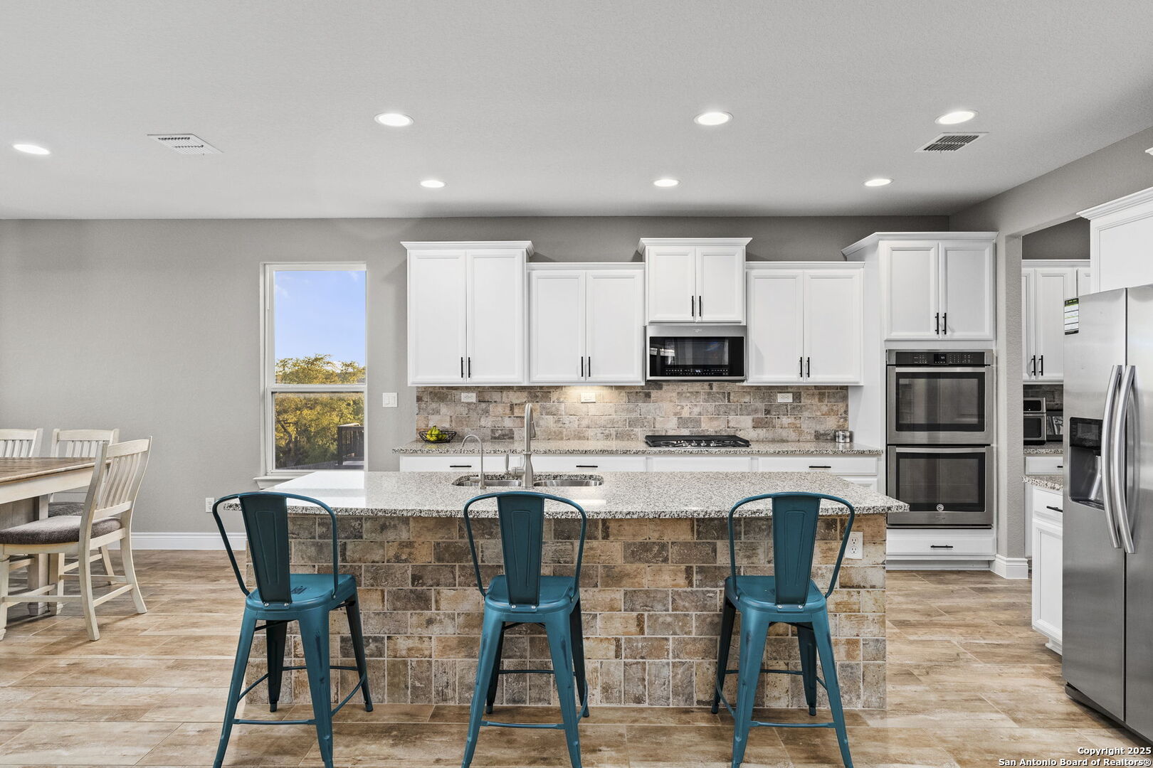 Kitchen with white cabinets, stone island, teal stools, and stainless steel appliances.