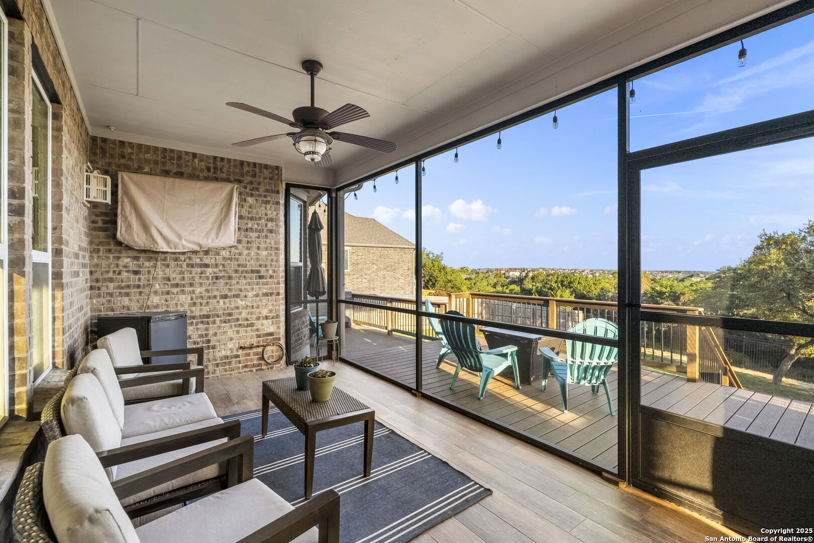 Screened-in patio with cushioned seating and ceiling fan, opening onto a deck with turquoise chairs.