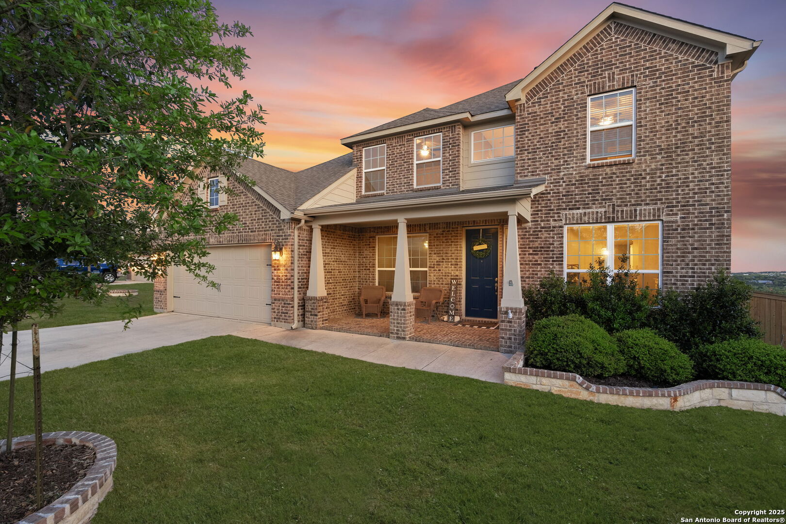 Two-story brick home with a covered porch and attached garage beneath a colorful dusk sky.