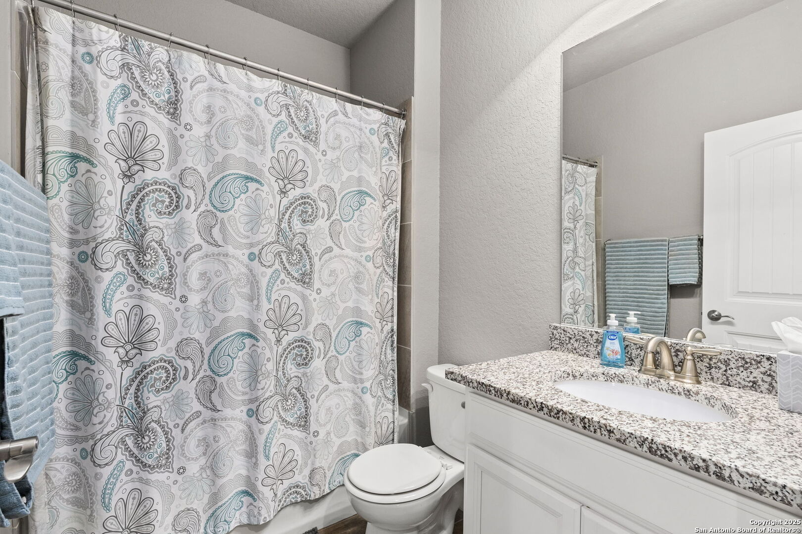 Bathroom with a patterned shower curtain, white toilet, and granite vanity.