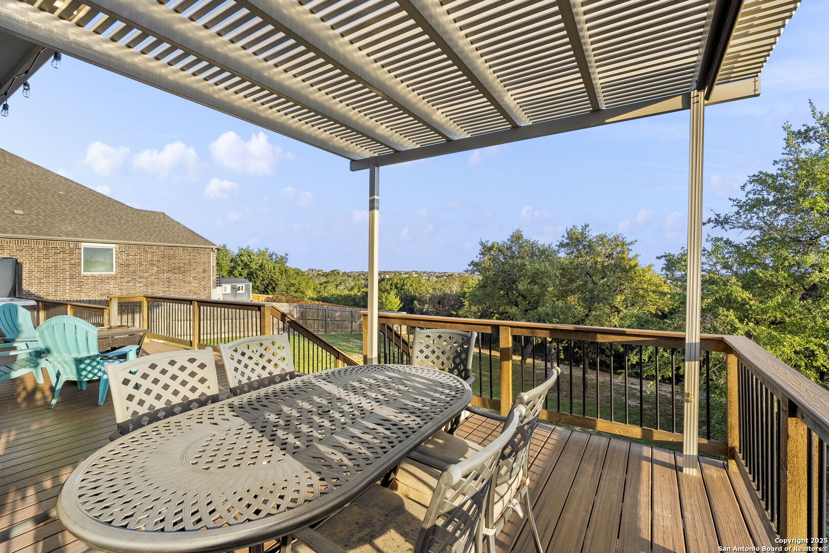 Backyard deck with a slatted pergola, outdoor dining set, and leafy tree views.